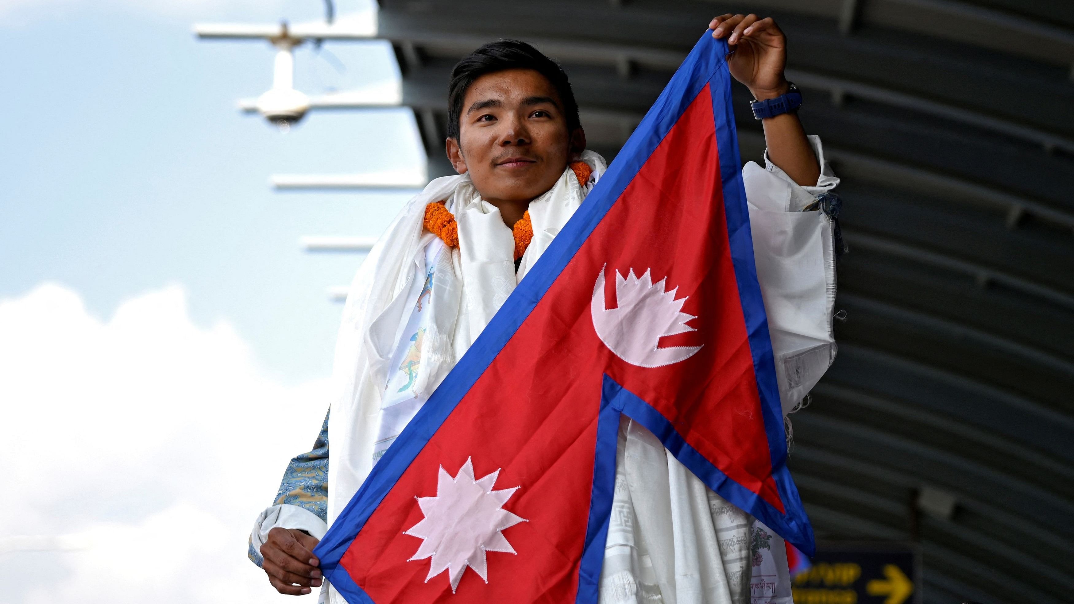 <div class="paragraphs"><p>Nima Rinji Sherpa, who claims the record for youngest person to scale world's 14 highest peaks, holds a national flag upon his arrival at the airport during a welcoming ceremony in Kathmandu, Nepal, October 14, 2024.</p></div>