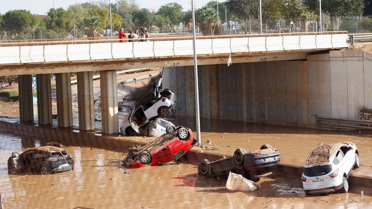 <div class="paragraphs"><p>People stand on a bridge over damaged cars on a mud-covered road in the aftermath of torrential rains that caused flooding, in Picanya, Spain, October 31, 2024.</p></div>