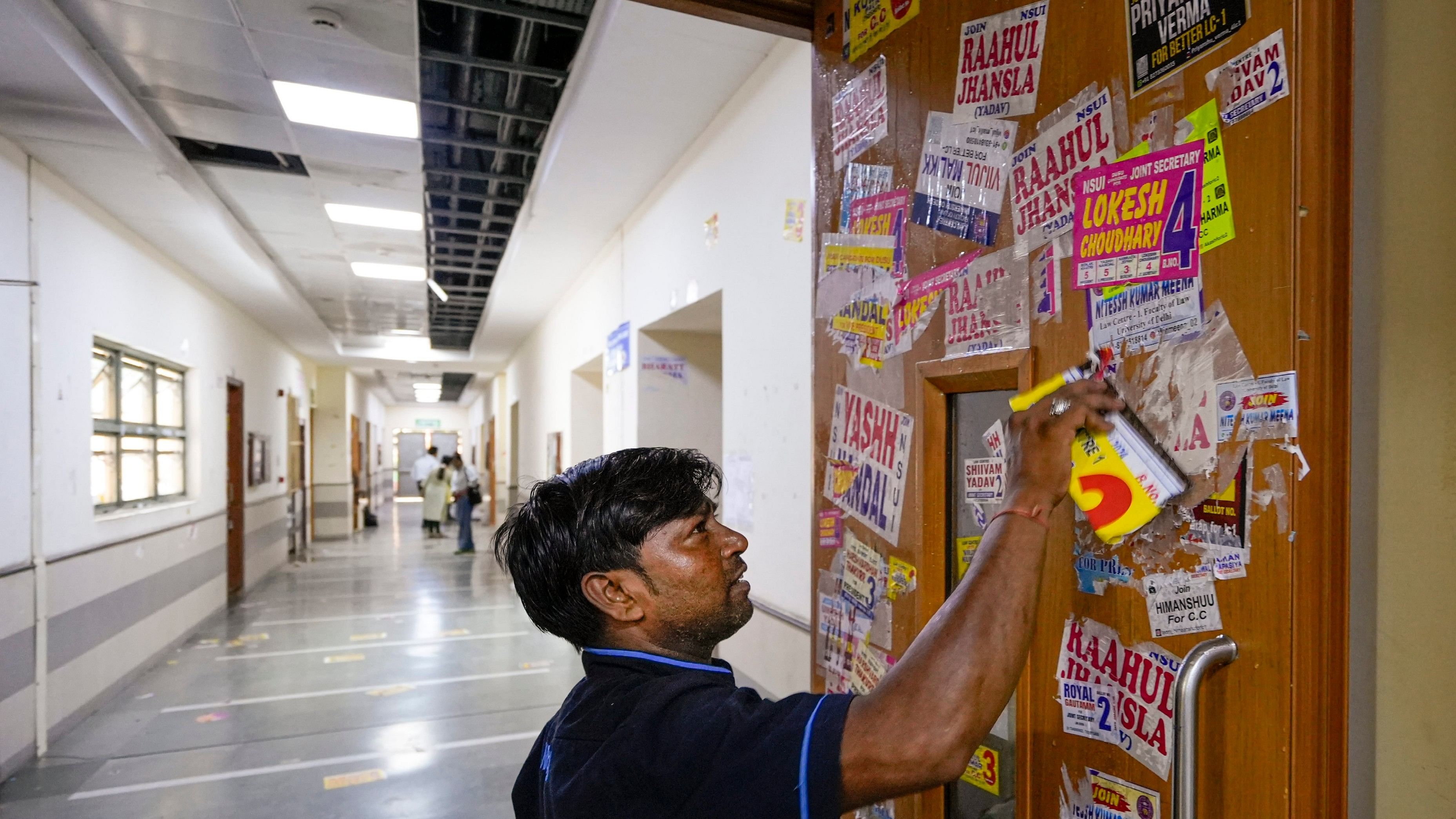 <div class="paragraphs"><p>A worker removes posters from the door of a classroom during the Delhi University Students' Union (DUSU) polls 2024, at Campus Law Centre, in New Delhi. The Delhi High Court had halted counting of votes of DUSU elections till the posters, spraypaints and graffitis are removed and public properties are restored. </p></div>