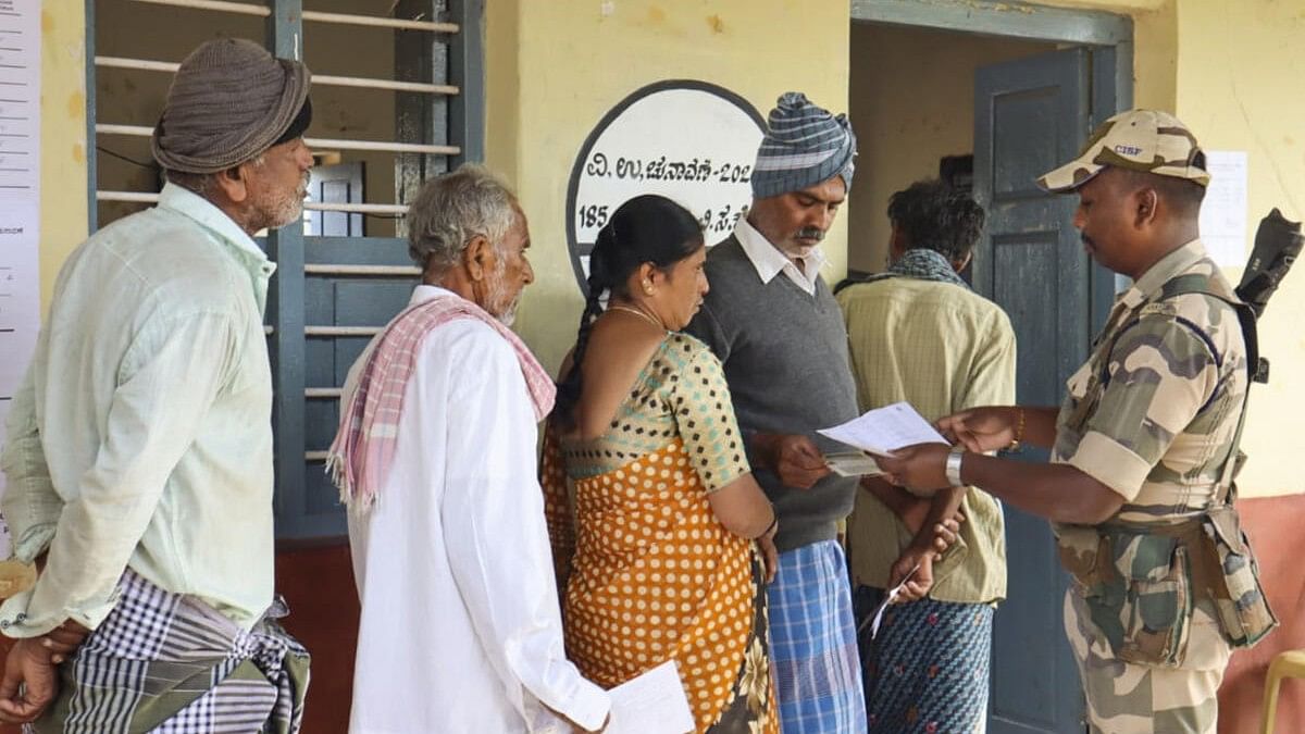 <div class="paragraphs"><p>A security personnel checks voter ID as voters wait to cast votes at a polling station during the Channapatna Assembly bypoll.&nbsp;</p></div>