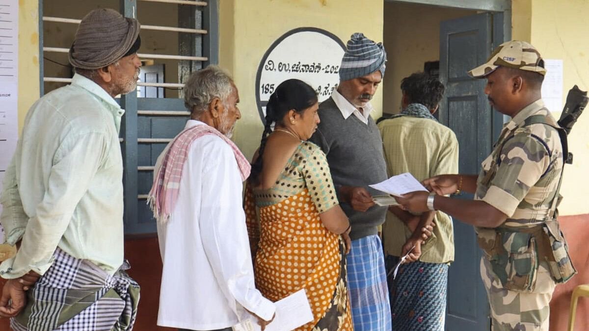 <div class="paragraphs"><p>A security personnel checks voter ID as voters wait to cast votes at a polling station during the Channapatna Assembly by-poll, Karnataka.</p></div>