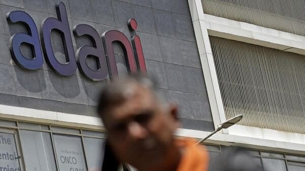 <div class="paragraphs"><p>A man on phone walks past Adani signage of a residential cum commercial tower in Mumbai. Representative image.</p></div>