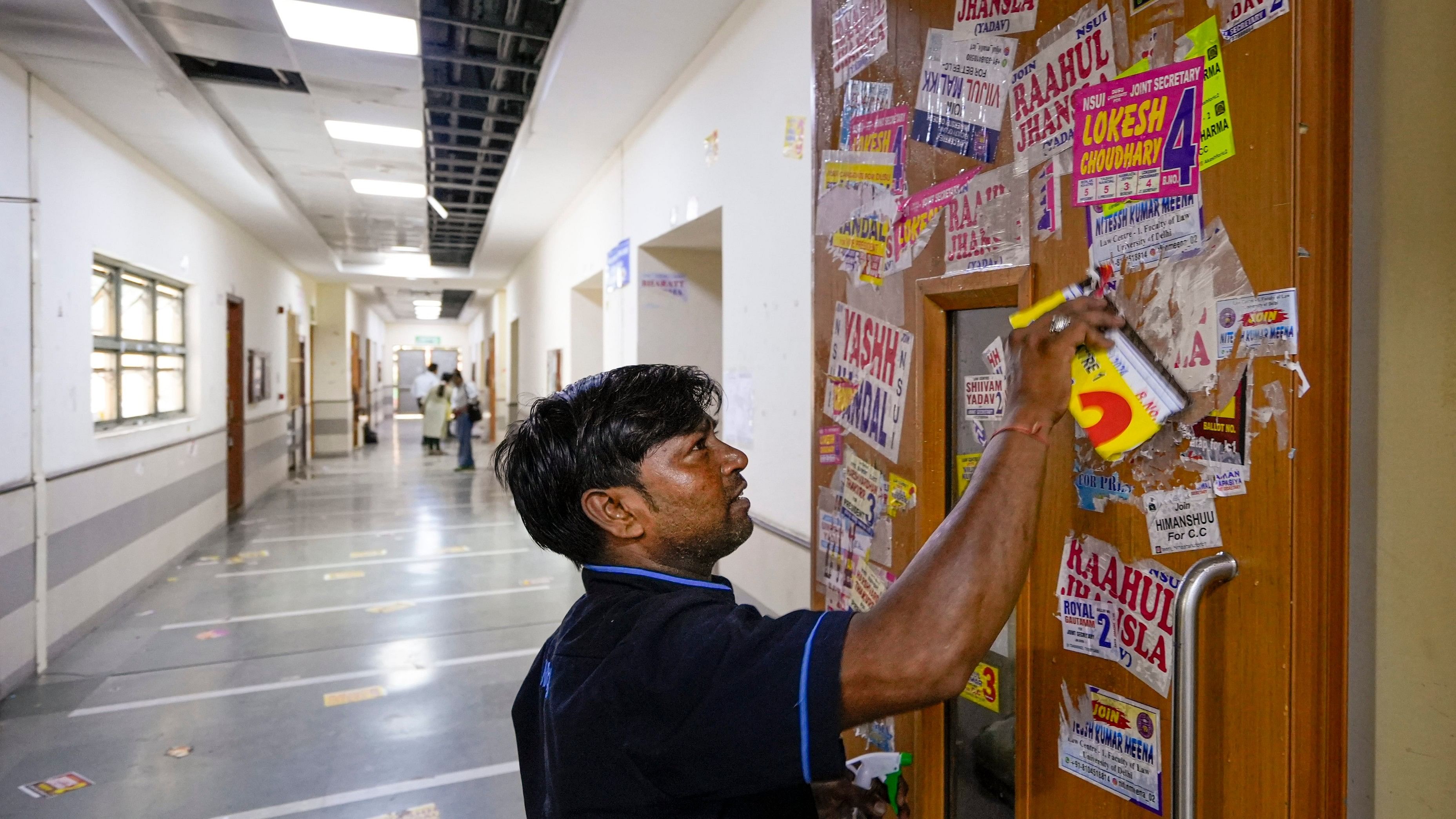 <div class="paragraphs"><p>A worker removes posters from the door of a classroom during the Delhi University Students' Union (DUSU) polls 2024 at Campus Law Centre in New Delhi.&nbsp;</p></div>