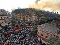 Local people gather on the road as fire personnel douse a major fire fire that broke out at a multi-storeyed building on Park Street in Kolkata on Tuesday. PTI