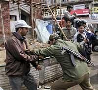 A policeman charging on a striking goverment employee during a protest march at Lal Chowk in Srinagar on Monday. PTI Photo