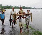 desperate measure : A man carries a child on a cot as villagers wade through a flooded road after the Ganga overflowed in Kanshi Ram Nagar near Agra on Sunday. pti