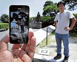 A man stands next to a tiny black and white panel to have his picture taken and displayed including, the animated image of a girl, through an iPhone application at the famous spot of Kanichi and Omiya in Atami, southwest of Tokyo. AFP