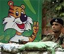 A security officer stands guard next to a poster showing Shera, the mascot for the Commonwealth Games on a street in New Delhi on Wednesday. AP