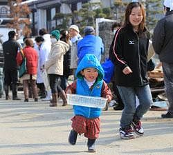 A toddler carries an empty basket and runs by a long queue of people outside a make-shift distribution center to pick up food and water in Ishinomaki, Miyagi Prefecture, one of the hardest tsunami stricken cities in Japan's northeast Pacific coast following the March 11 earthquake, Tuesday, March 22, 2011. AP
