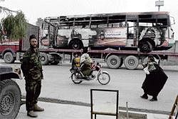 day is ahead An Afghan National Army soldier stands guard at the entrance of the Zargona Ana High School for Girls as a burned-out bus destroyed during recently demonstrations is trucked past in Kandahar. nyt
