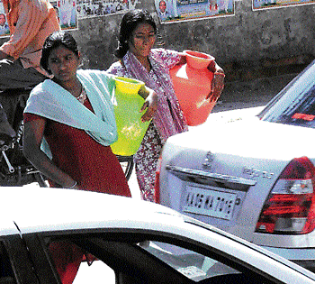 Women weave through heavy traffic on Queens Road to  carry water to their homes. DH photo