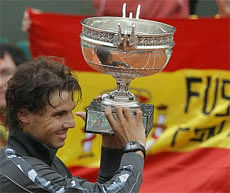 The Spanish flag is seen in the background as Rafael Nadal of Spain holds the trophy after winning the mens final match against Novak Djokovic of Serbia at the French Open tennis tournament in Roland Garros stadium in Paris, Monday June 11, 2012. Rain suspended the final making it the first French Open not to end on Sunday since 1973. Nadal won in four sets 6-4, 6-3, 2-6, 7-5, passing Sweden's Bjorn Borg as the all-time record-holder for French Open titles. (AP Photo)