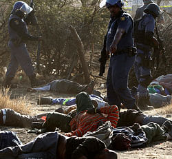 A policeman gestures in front of some of the dead miners after they were shot outside a South African mine in Rustenburg, 100 km (62 miles) northwest of Johannesburg, August 16, 2012. South African police opened fire on Thursday against thousands of striking miners armed with machetes and sticks at Lonmin's Marikana platinum mine, leaving several bloodied corpses lying on the ground. A Reuters cameraman said he saw at least seven bodies after the shooting, which occurred when police laying out barricades of barbed wire were outflanked by some of an estimated 3,000 miners massed on a rocky outcrop near the mine, 100 km (60 miles) northwest of Johannesburg. REUTERS