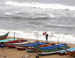 An Indian man tries to hold on to his umbrella in strong winds, as he stands beside fishing boats on the Bay of Bengal coast as tidal waves approach the shore in Chennai, India, Tuesday, Oct. 30, 2012. The Indian Meteorological Department has advised fishermen not to venture into the open seas with Cyclone Nilam reported swirling about 450 kilometers (281) miles south east of here Tuesday. (AP Photo)