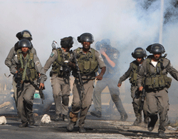 Israeli border guards run through a cloud of tear gas as they clash with Palestinian protesters in the West Bank city of Nablus on November 21, 2012, during a protest against the ongoing Israeli military offensive on the Gaza Strip. A new wave of Israeli raids on Gaza killed 11 people, including a child who died when the tower housing AFP's office was struck for the second time in 24 hours. AFP