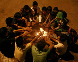 People warm themselves near a bonfire in Thane on Saturday night. PTI