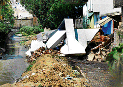 the Crash: A house adjacent to the stormwater drainage collapsed during the construction of the side wall at Okalipuram in  Bangalore on Monday. dh Photo