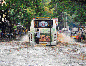 Waterway: A passenger struggles to cling on to the ladder of a bus passing through the flooded RMP Link Road in Davanagere on Monday afternoon. DH Photo