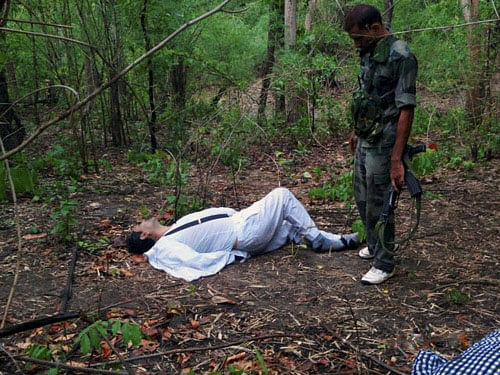 A security person stands near the body of one of the victims of Saturday's Maoist attack in a densely forested area in Bastar, about 345 kilometers (215 miles) south of Raipur, Chhattisgarh state, India, Sunday, May 26, 2013. Officials reacted with outrage Sunday to an audacious attack by about 200 suspected Maoist rebels who set off a roadside bomb and opened fire on a convoy carrying Indian ruling Congress party leaders and members in an eastern state, killing at least 24 people and wounding 37 others. AP photo