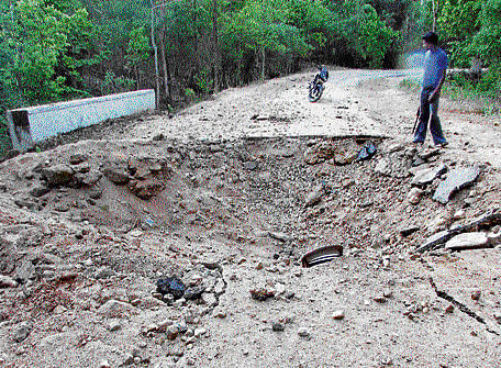An unidentified man stands near the crater created on the road after May 25 Maoist land mine attack in a densely forested area in Bastar District. ap