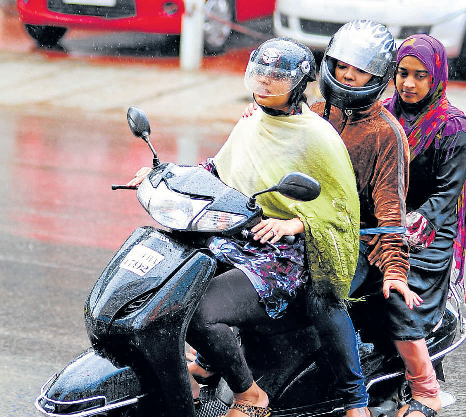 Youngsters on triple ride in heavy rain at Richmond Road in Bangalore on Monday evening. DH Photo