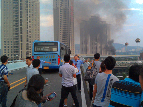 Bus drivers try to keep passengers away from the direction of a bus that burst into flames in Xiamen, southeast China's Fujian Province on Friday, June 7, 2013. An express bus burst into flames on an elevated road in southeastern China on Friday, killing 47 people, state media reported. (AP Photo)