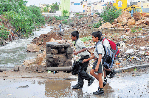 Life at risk: Schoolchildren walk next to the damaged wall of a stromwater drain at  Ittamadu. Contractors hesitate to take up SWD projects for varied reasons. dh photo