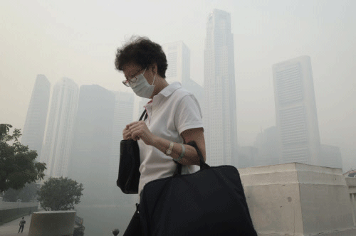 A woman wears a mask in a haze blanketed the Singapore Central Business District, or CBD in the background on Thursday, June 20, 2013. A smoky haze triggered by forest fires in neighboring Indonesia has caused air pollution to briefly hit its worst level in nearly 16 years in Singapore. (AP Photo