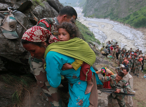Soldiers assist a woman carrying a child on her back during rescue operations in Govindghat in the Himalayan state of Uttarakhand June 23, 2013. Flash floods and landslides unleashed by early monsoon rains have killed at least 560 people in Uttarakhand and left tens of thousands missing, officials said on Saturday, with the death toll expected to rise significantly. Houses and small apartment blocks on the banks of the Ganges, India's longest river and sacred to Hindus, have toppled into the rushing, swollen waters and been swept away with cars and trucks. REUTERS/