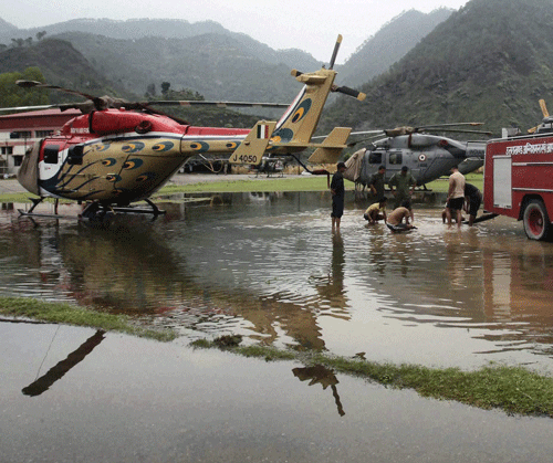 Fire fighters busy to clear water around parked relief helicopters after rains at Gauchar airbase on Monday. PTI Photo