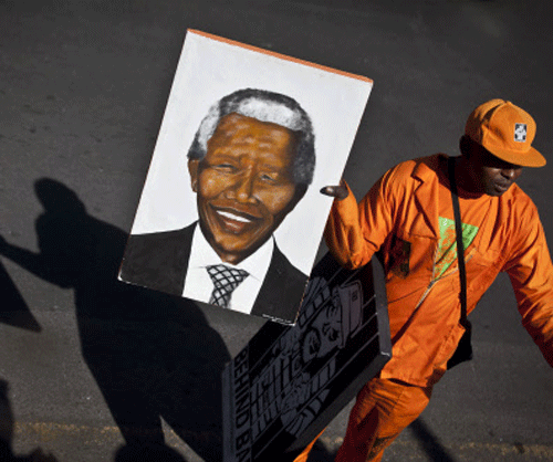 An arriving wellwisher carries a portrait of Nelson Mandela as he walks down the street outside the entrance to the Mediclinic Heart Hospital where former South African President Nelson Mandela is being treated in Pretoria, South Africa Thursday, June 27, 2013. Makaziwe Mandela, daughter of Nelson Mandela, said Thursday he is in very critical condition but is still opening his eyes and reacting to touch at the South African hospital where he is being treated. AP Photo.