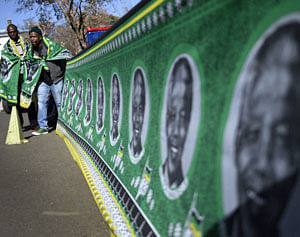 Men stand next to a banner covered with portraits of Nelson Mandela to a wall outside the Medi-Clinic Heart Hospital, where the ailing former South African President is being treated, in Pretoria June 28, 2013. REUTERS