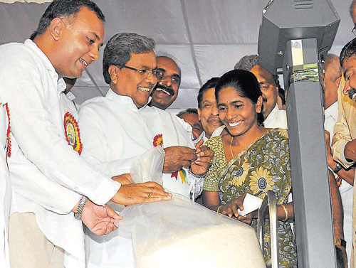 Welfare measure: Chief Minister Siddaramaiah distributes 30 kg rice to a beneficiary to mark the inauguration of the 'Anna Bhagya' scheme in the City on Wednesday. Food and Civil Supplies Minister Dinesh Gundurao is also with him. DH Photo