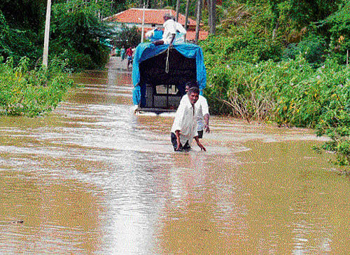 marooned: People of Kalasindha village pull a vehicle that was stranded in the flooded road following a breach in Hemavathi left bank canal near Vaddarahalli jackwell in Channarayapattana taluk on Sunday. DH Photo