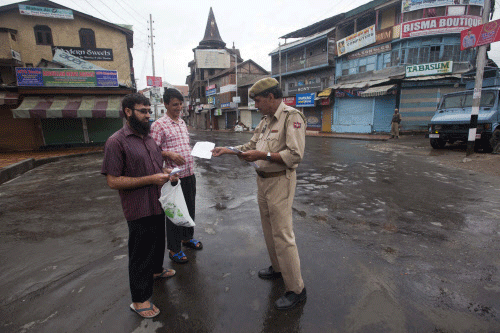Kashmiris shows medical prescriptions to an Indian police officer at a checkpoint during curfew in Srinagar, India, Saturday, July 20, 2013. A strict curfew continues for the second day in most of Indian-controlled Kashmir on Saturday, with thousands of troops fanning out across the region. The curfew was imposed a day after government forces on Thursday fatally shot four villagers. AP photo
