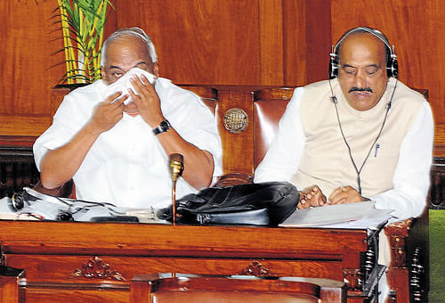 Legislator Ramesh Kumar wipes his tears in the Legislative Assembly on Tuesday, during a discussion on encroachment of government lands. Legislator Ashok Pattan is also with him. DH photo