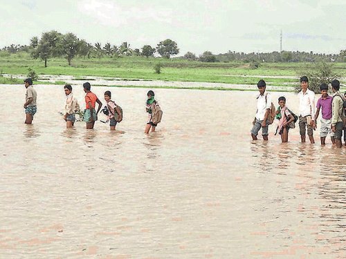 RAIN TRAVAILS: Road connectivity between Gudura-Marola villages in Haveri talukwas snapped as backwaters of River Varada submerged the road. Peoplewere seenwading through thewater to reach their destinations onWednesday. DH PHOTO