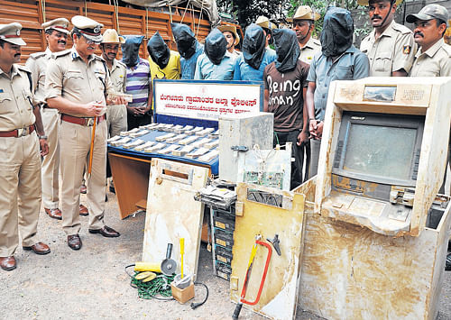 case cracked: The seven men (in hoods), who towed away ATMs containing huge amounts of cash, stand behind the recovered money and a teller machine. DH Photo