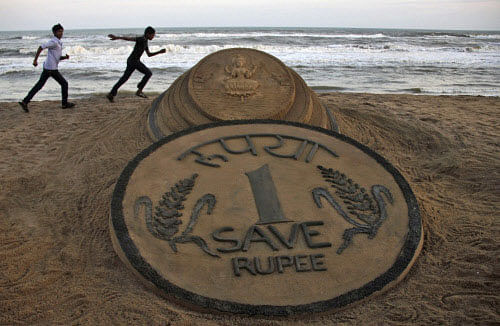 A camel owner walks past a sand sculpture of a rupee coin on a beach in Puri on Thursday. Reuters Image