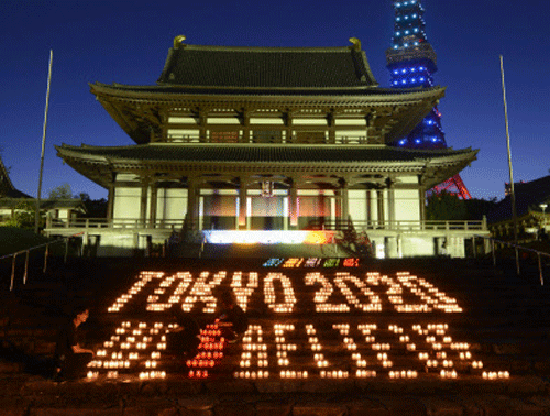 A message reading: 'Tokyo 2020 We believe' is lit up by candle lights in the compound of Zojoji Temple with the backdrop of Tokyo Tower illuminated in Olympic colors in Tokyo. AP Photo