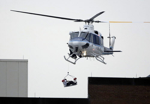 A helicopter pulls up an apparent shooting victim as it hovers over a rooftop on the Washington Navy Yard campus in Washington, September 16, 2013. Seven people were killed and five wounded in a shooting rampage on Monday at the U.S. Navy Yard, where one suspected gunman was killed and two other possible assailants were being sought, authorities said. The exact number of dead and wounded fluctuated in the hours following the mass shooting, which took place less than three miles (4 km) from the White House. REUTERS