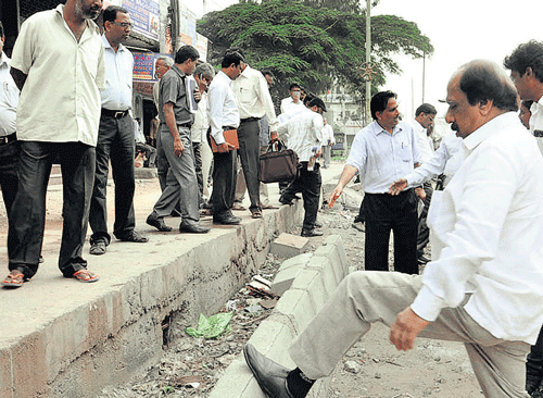 here we go: Mayor Satyanarayana kicks a footpath wall that gave in immediately, exposing substandard work, on Mysore Road on Friday. dh photo