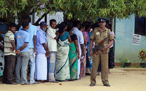 A Sri Lankan police officer stands guard as ethnic Tamils wait to cast their vote at a polling station during the northern provincial council election in Jaffna, Sri Lanka, Saturday, Sept. 21, 2013. Ethnic Tamil voters in Sri Lanka's war-ravaged north went to the polls Saturday to form their first functioning provincial government, hoping it is the first step toward wider regional autonomy after decades of peaceful struggle and a bloody civil war. (AP Photo