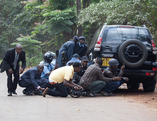 Police officers and members of the media take cover at a distance from the Westgate Shopping Centre after continuous gunfire was heard coming from the mall in Nairobi September 23, 2013. Thick smoke poured from the besieged Nairobi mall where Kenyan officials said their forces were closing in on Islamists holding hostages on Monday, three days after a raid by Somalia's al Shabaab killed at least 62 people. It remained unclear how many gunmen and hostages were still cornered in the Westgate shopping centre, two hours after a series of loud explosions and gunfire were followed by a plume of black smoke, that grew in volume from one part of the complex. REUTERS
