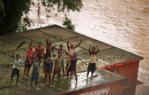 People wait for relief material on the top of a thatch in a flooded locality after heavy rains in the aftermath of Cyclone Phailin in Balasore on Monday. PTI Photo
