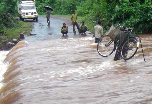 A cyclist crosses the road by holding his cycle as flood water flowing over Dasarathpur road in Jajpur on Tuesday. PTI Photo