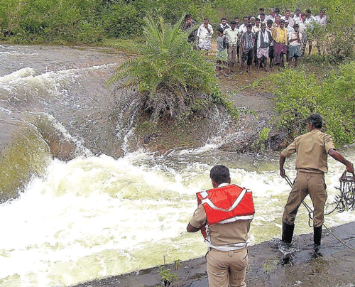 Fire personnel try to retrieve the body of Raghavendra who was washed away after a tank breached at Hanagal village in Arakalgud taluk, Hassan district, on Sunday.  dh photo