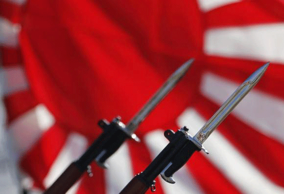 Bayonets attached to rifles used by Japanese Self-Defense Forces are seen in front of Japan's rising sun flag, which is used by the forces, during the annual troop review ceremony at Asaka Base in Asaka, near Tokyo October 27, 2013.  Reuters file image