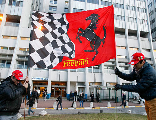 Fans fix a Ferrari flag in the ground in front of the CHU Nord hospital emergency unit in Grenoble, French Alps, where retired seven-times Formula One world champion Michael Schumacher is hospitalized after a ski accident, December 31, 2013. The medical condition of seven-times Formula One world champion Michael Schumacher is slightly better on Tuesday following a second operation during the night to treat head injuries he sustained in a skiing accident, doctors said. Schumacher was admitted to hospital on Sunday suffering head injuries in an off-piste skiing accident in the French Alps resort of Meribel. REUTERS