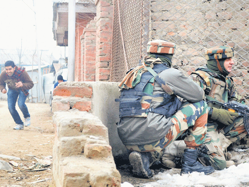 RUNNING FOR cover: A youth runs for cover as Army soldiers take position outside the house where militants were holed up  during an encounter at Dooru in Sopore on Monday. Pti